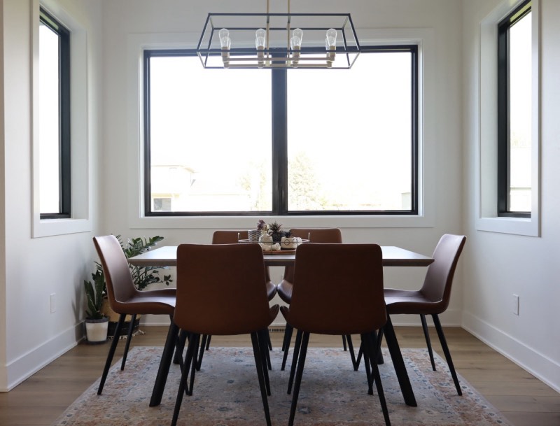 Dining area with three black-framed windows, a linear cage chandelier and white oak flooring