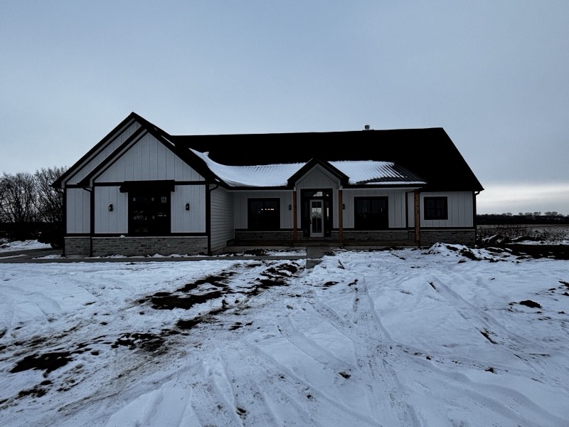 Board and batten farmhouse ranch with stone skirt and cedar porch posts, photographed in snow at dusk