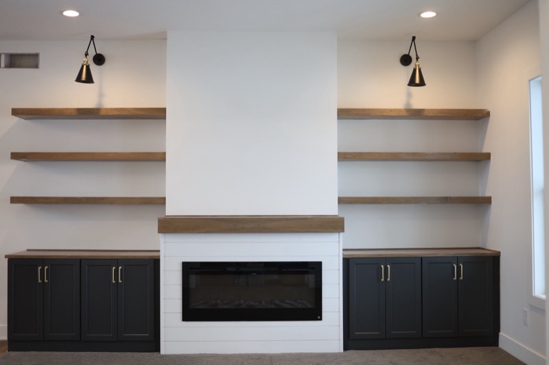 Shiplap fireplace with a timber mantel flanked by black cabinetry, floating shelves and swing-arm sconces