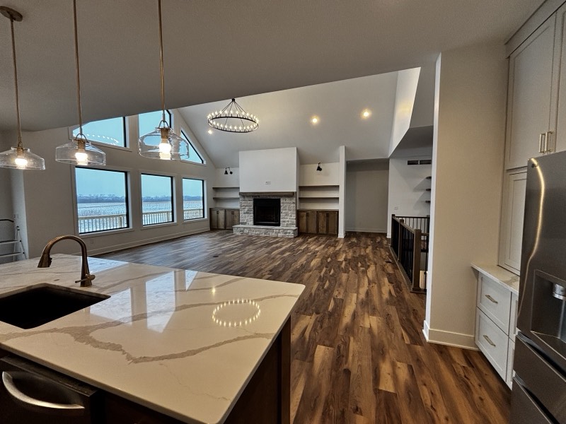 Kitchen island looking across an open great room to a stone fireplace and a wall of windows over an Iowa field