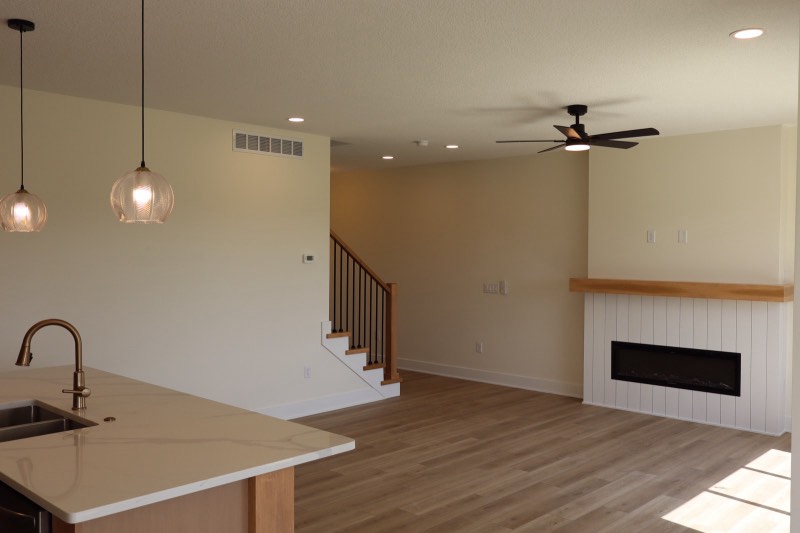 Great room with a white shiplap linear fireplace, solid oak mantel, staircase with iron balusters and a kitchen island