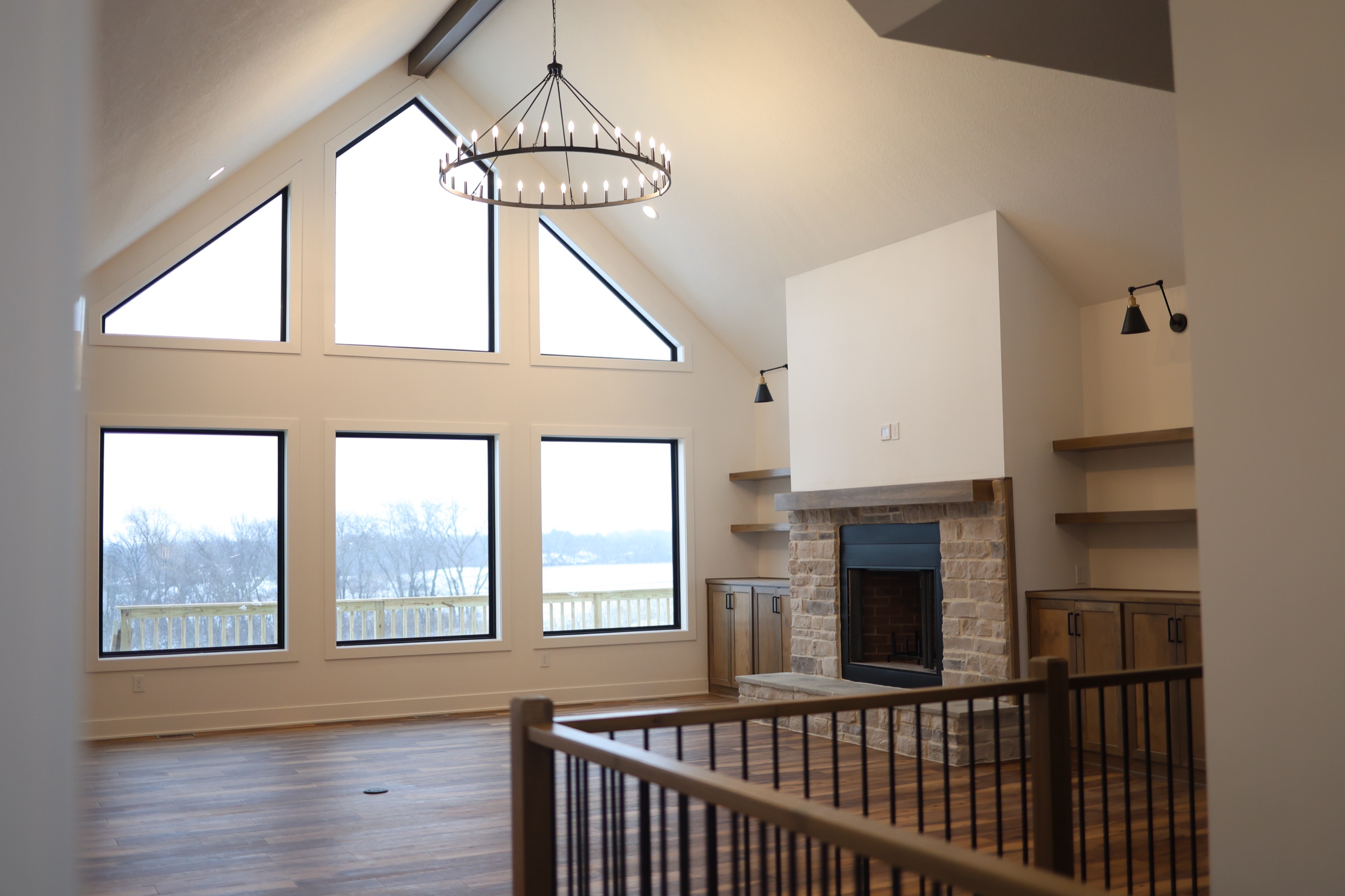 Vaulted great room with gable windows, a stone fireplace and a wagon-wheel chandelier in a custom home built by Stone + Timber Homes in Central Iowa