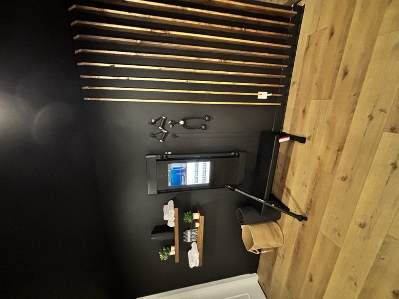 Home gym with a stained slat feature wall, black walls, floating shelves and a wall-mounted trainer