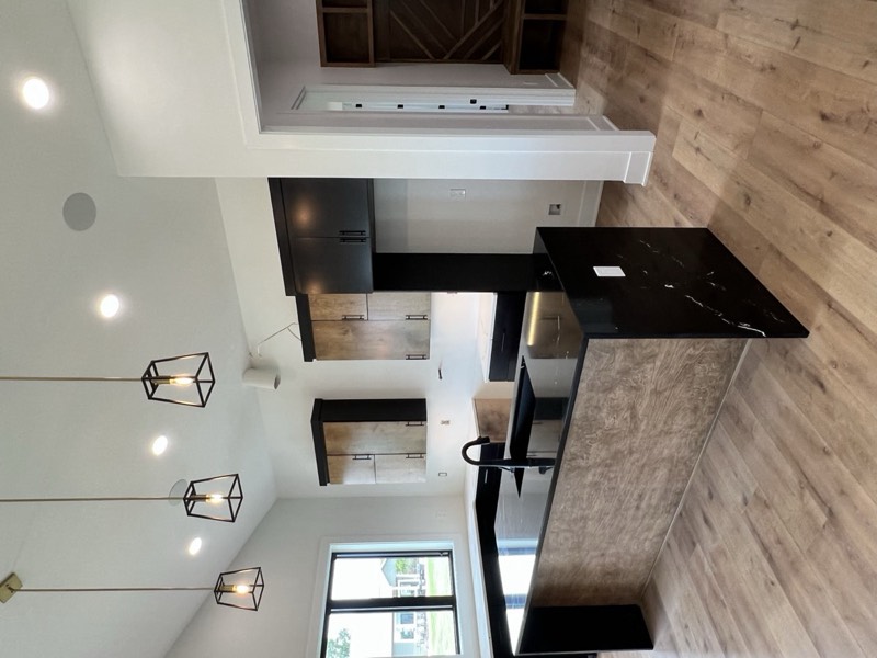 Kitchen with a black waterfall quartz island, mixed black and stained cabinetry and cage pendants