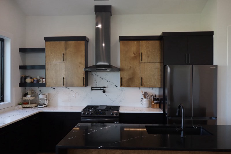 Kitchen with black lower cabinets, white oak uppers, marble-look quartz and a pot filler