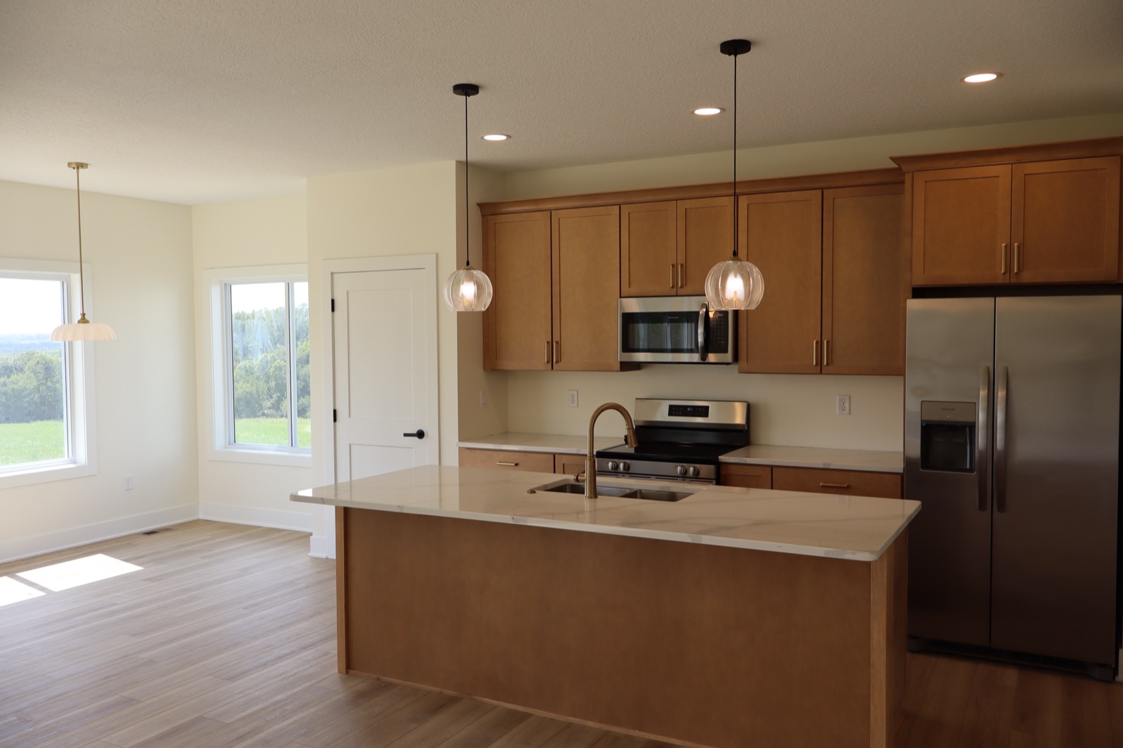 Open kitchen and dining with maple cabinetry, quartz island and windows onto open ground in a Central Iowa home built by Stone + Timber Homes