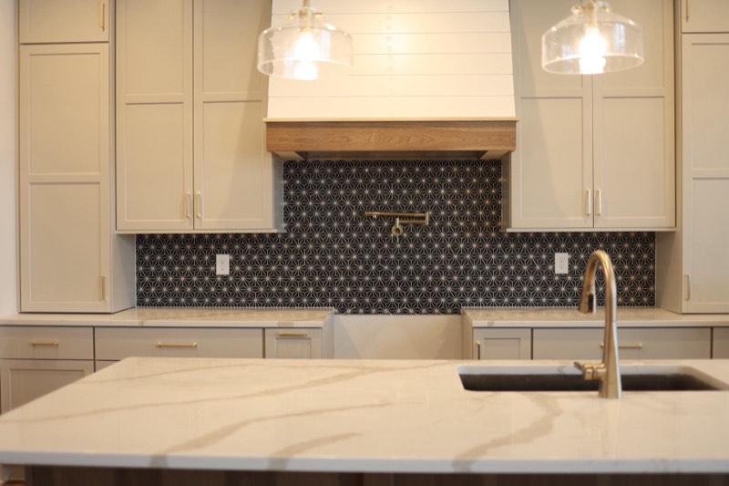 Custom kitchen with a shiplap hood, timber band, black patterned tile backsplash and a long quartz island