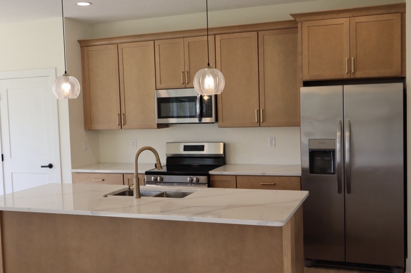 Maple kitchen with a quartz island, brushed gold faucet, ribbed glass globe pendants and stainless appliances