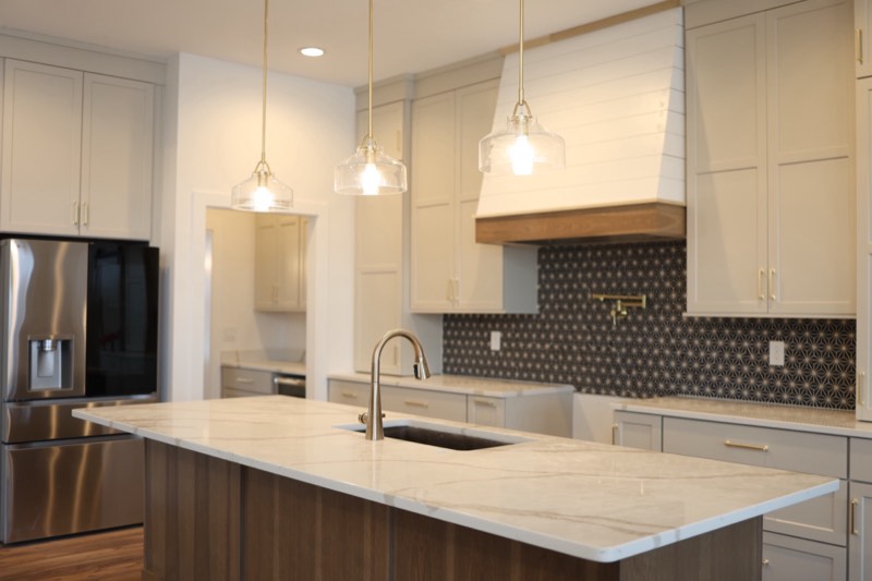 Kitchen island in marble-look quartz under three clear glass dome pendants, with a shiplap hood beyond