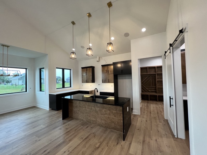 Vaulted kitchen and dining with a black waterfall island, cage pendants, barn door and custom mudroom lockers beyond