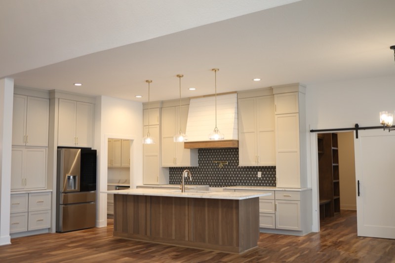 Wide view of a custom kitchen with a shiplap hood, patterned tile backsplash, walnut island and a barn door into the pantry