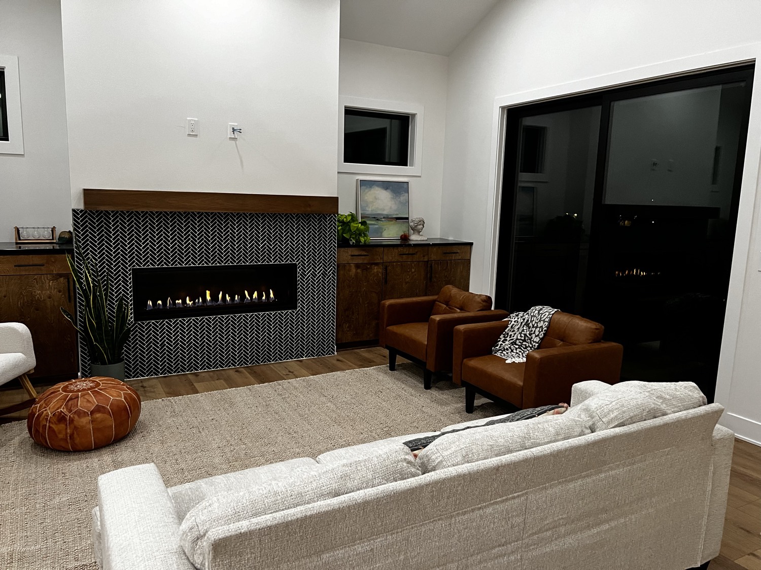 Furnished living room with a linear herringbone tile fireplace, leather chairs and a sectional in a completed Stone + Timber home