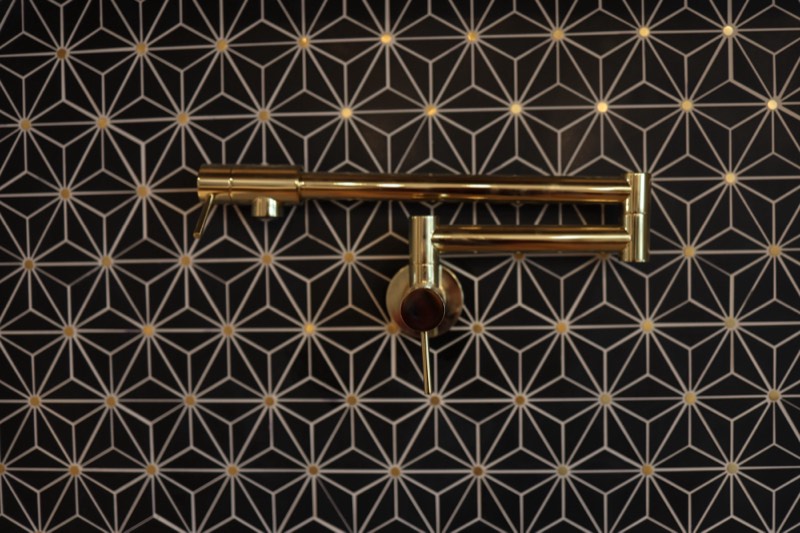 Polished brass pot filler mounted on a black and gold star-pattern tile backsplash