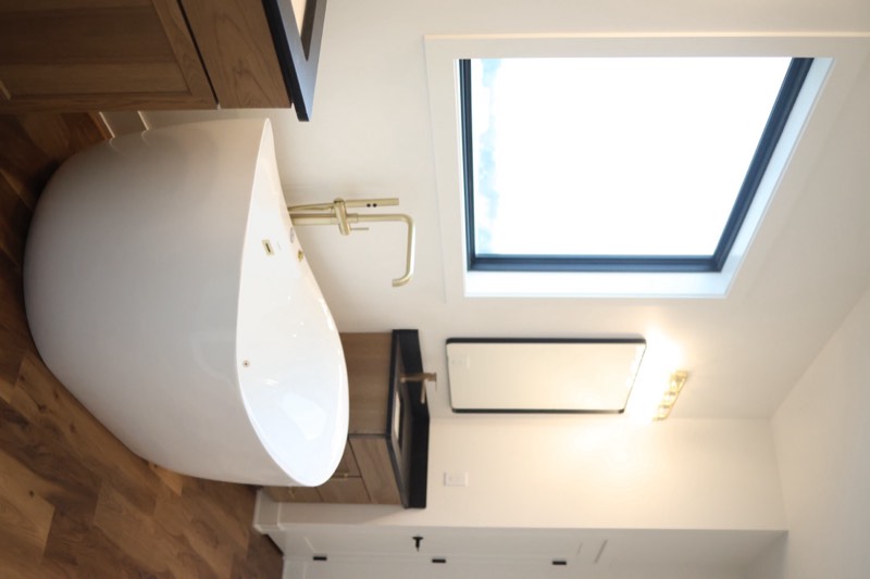 Primary bathroom with dual walnut vanities, black quartz tops, gold fixtures and a freestanding tub under a window