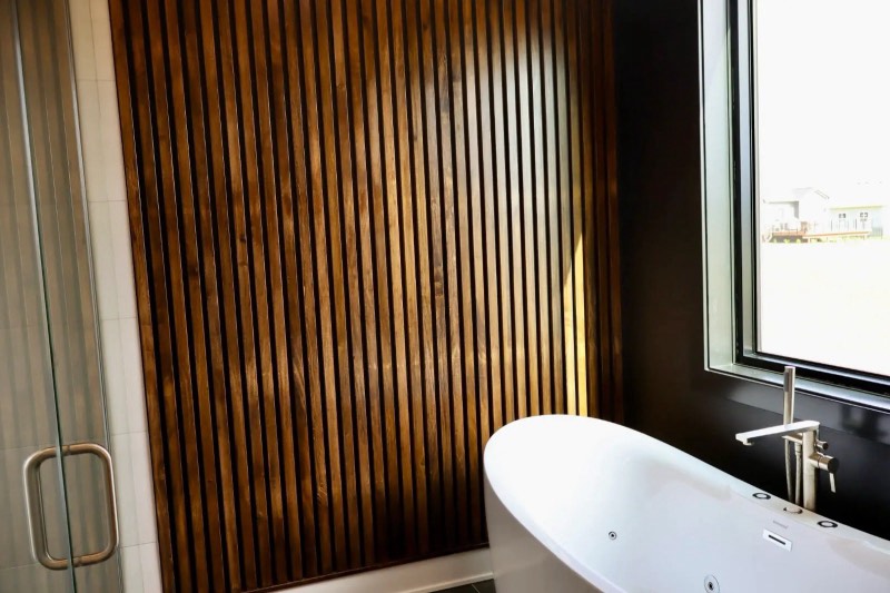 Primary bathroom with a stained wood slat feature wall, freestanding tub and glass shower