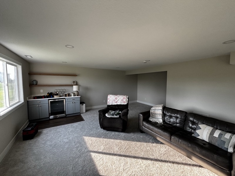 Finished basement family room with a wet bar, beverage fridge, floating shelves and an egress window