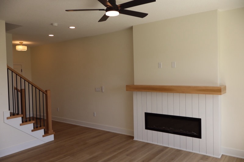 White vertical shiplap fireplace surround with a thick solid oak mantel beside an iron baluster staircase