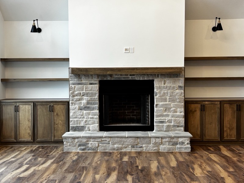 Stone fireplace with a rough-sawn timber mantel flanked by built-in cabinets and floating shelves