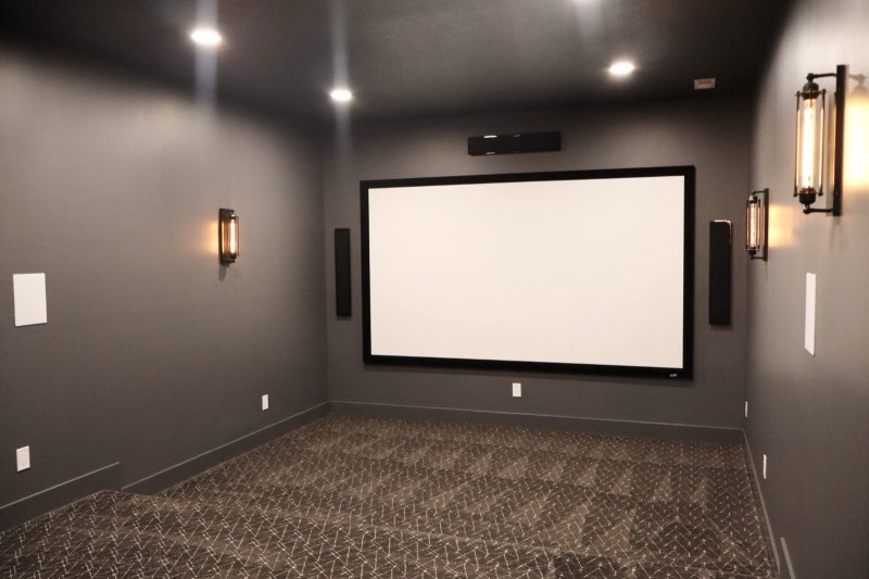 Finished lower-level home theater with projection screen, in-wall speakers, sconces and patterned carpet