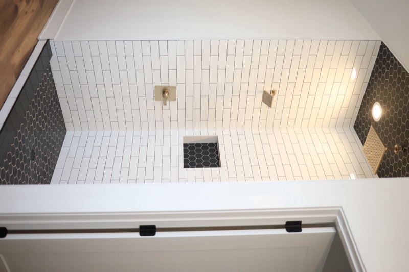 Walk-in tile shower with white subway tile, black hexagon side walls, two rain heads and recessed niches